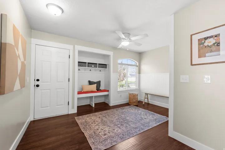 Wood-finish flooring, built-in bench with storage cubbies and coat hooks, arched window, ceiling fan, and wainscoting