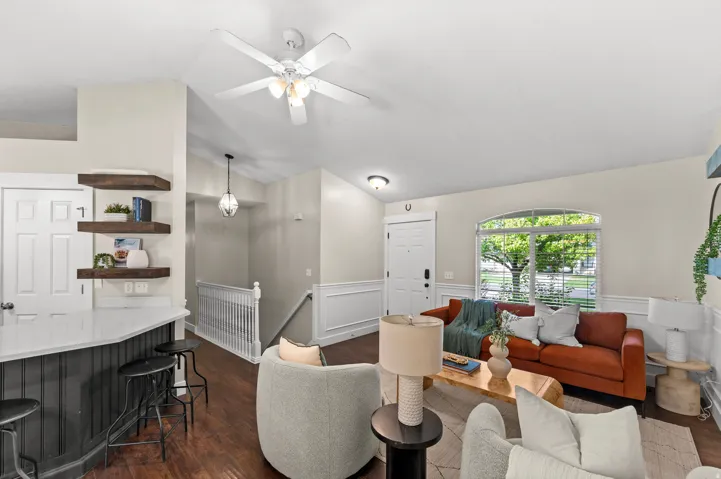 Wood-finish flooring throughout, white paneled entry door, white wainscoting, and a ceiling fan with integrated lighting