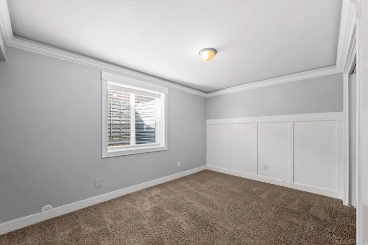 Board and batten accent wall, neutral wall color, crown molding, window with blinds, and carpeted flooring