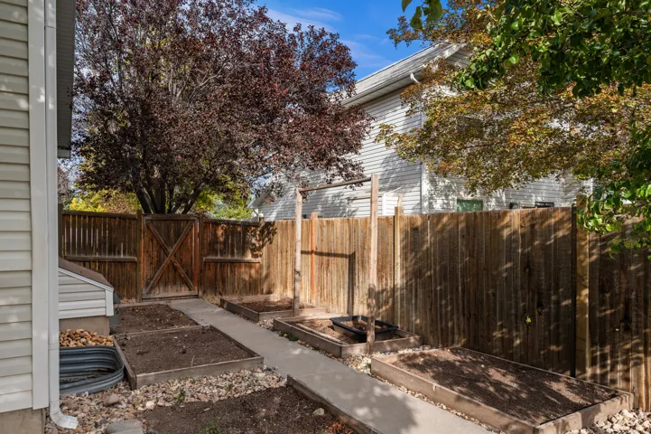 Backyard featuring raised garden beds, a concrete pathway, and a wood privacy fence with a gate