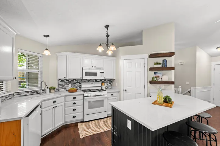 White cabinetry with black hardware, white countertops, stainless steel sink with gooseneck faucet, tiled backsplash, and wood-finish flooring