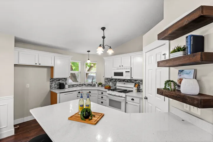 White cabinetry, wood-finish flooring, white appliances, corner sink, and white countertops