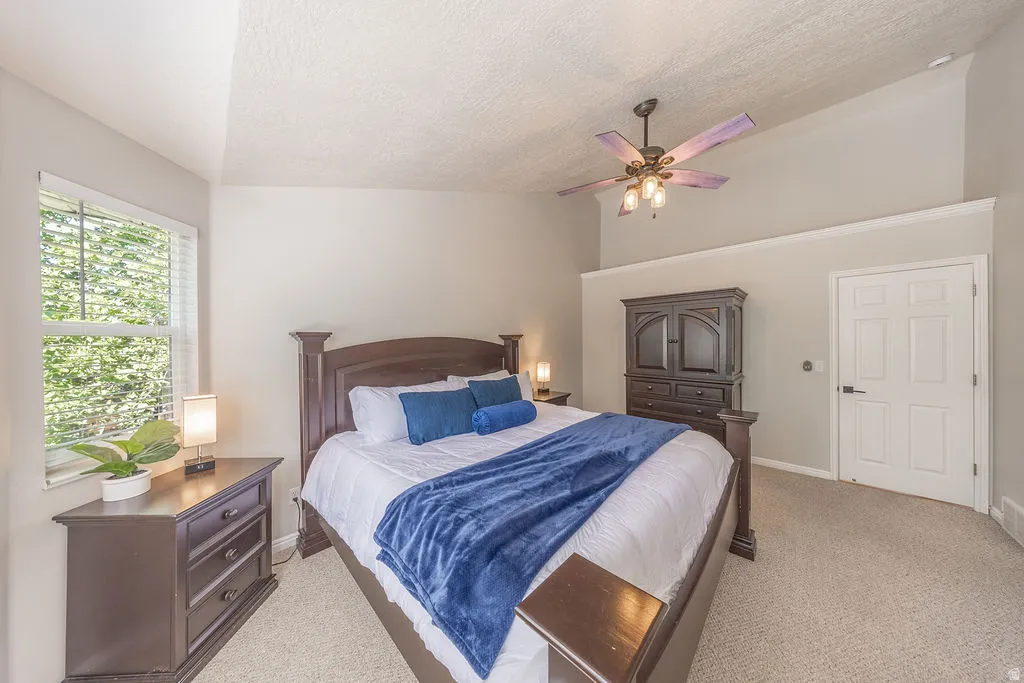 Vaulted ceiling with crown molding, ceiling fan, carpeted flooring, and a multi-pane window