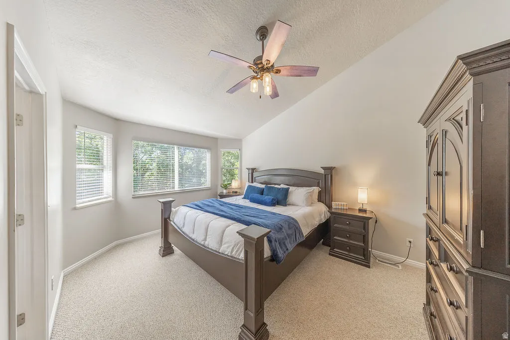 Vaulted ceiling, multiple windows, ceiling fan with integrated lighting, light-toned carpet flooring, and a built-in closet