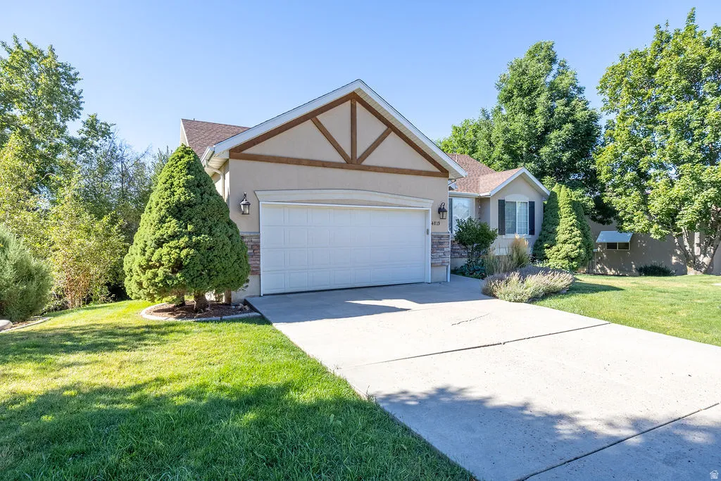 Stucco exterior with stone accenting, wood-beam gable detail, double garage, and a concrete driveway
