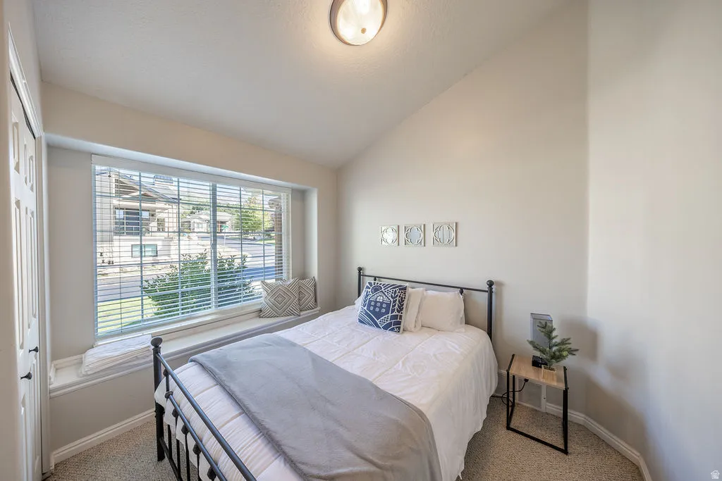 Carpeted room featuring a large window with blinds, a window seat, and a vaulted ceiling