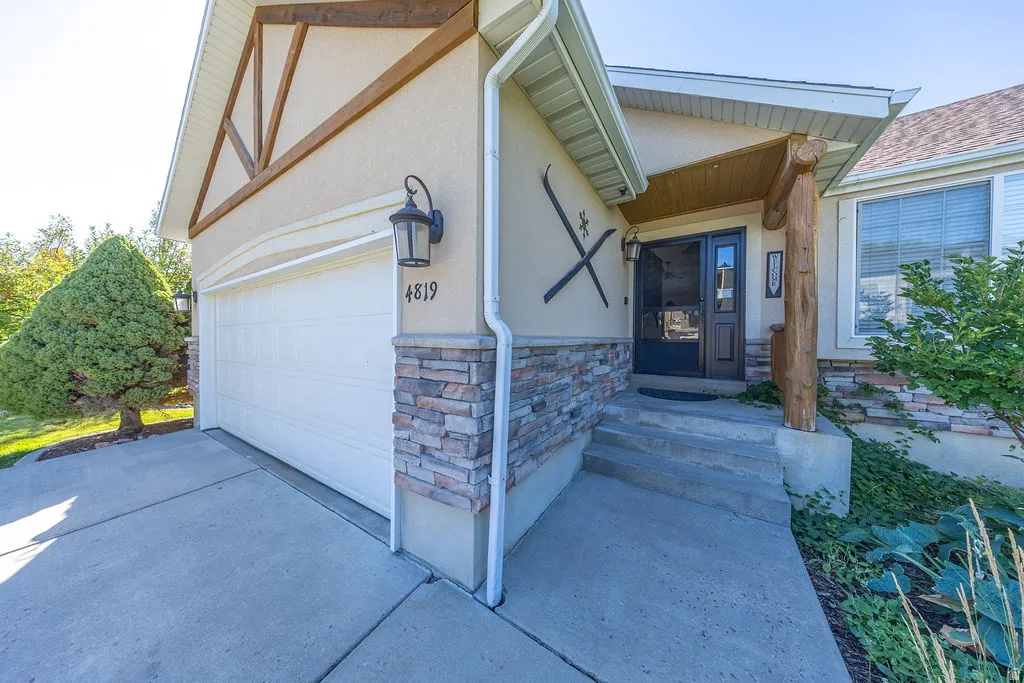 Stucco exterior with wood trim accents, stone veneer detailing, covered entry porch with rustic wood column, and an attached garage with a concrete driveway