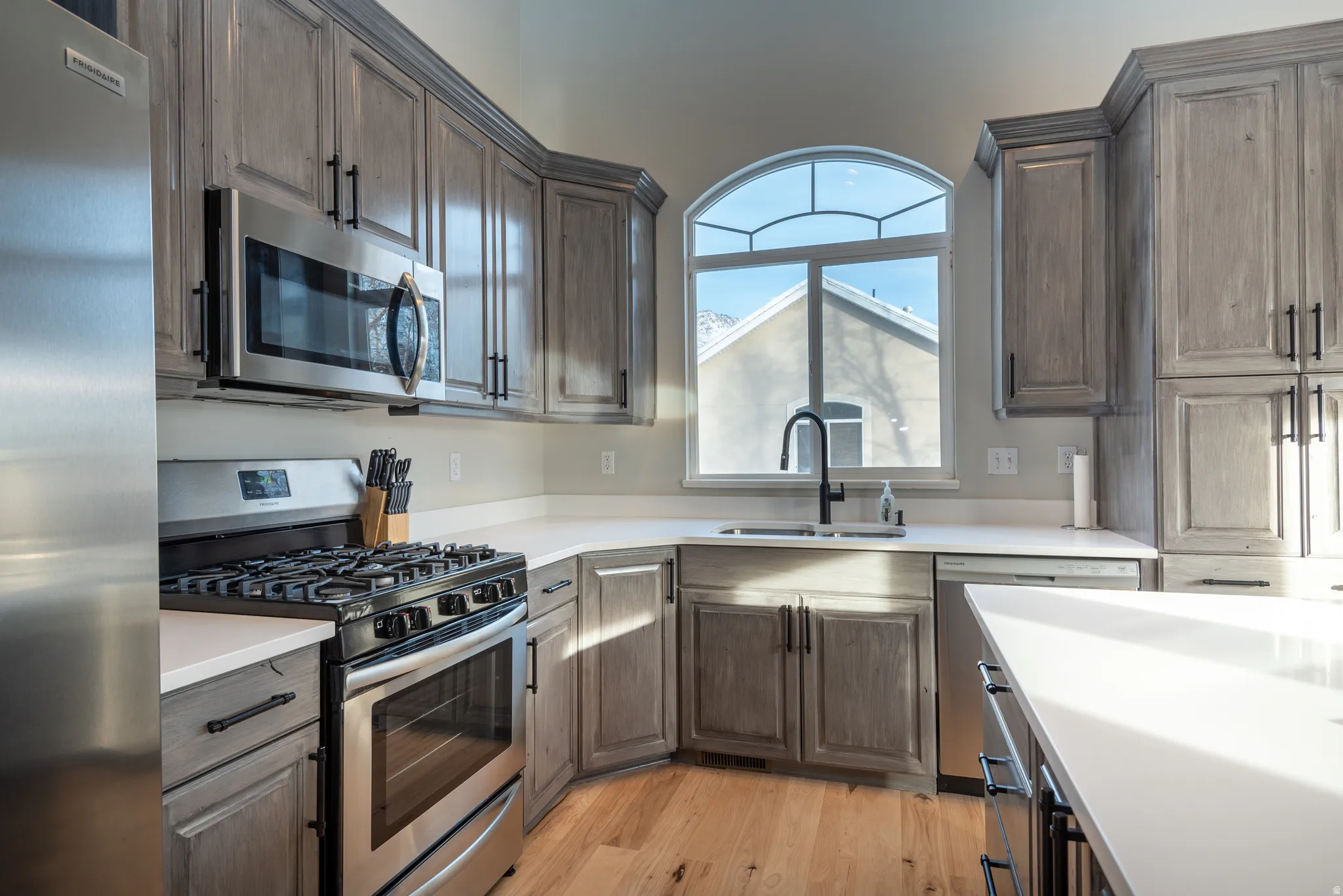 Kitchen featuring wood-finish flooring, light-toned cabinetry, stainless steel appliances, white countertops, and an arched window