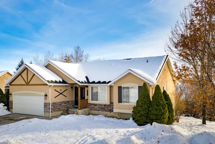 Stucco exterior with stone accent, front entry with wood railing, attached garage, and evergreen landscaping