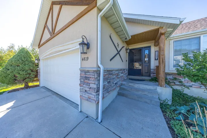 Stucco exterior with wood trim accents, stone veneer detailing, covered entry porch with rustic wood column, and an attached garage with a concrete driveway