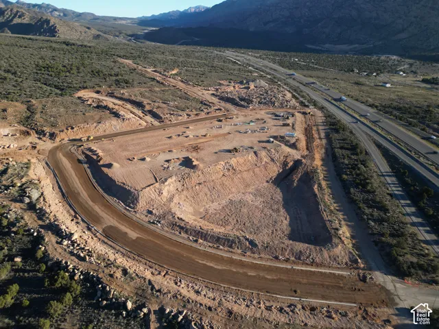Graded land parcel with established roadbed, surrounded by natural desert terrain, adjacent to a multi-lane highway, with distant mountains
