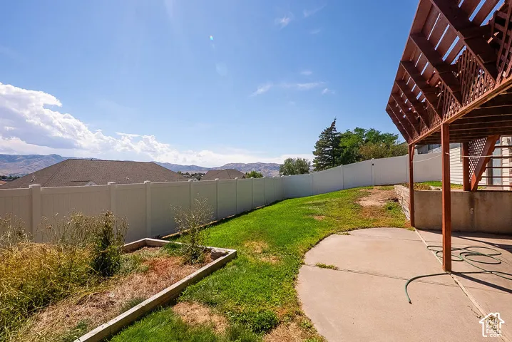 Expansive backyard featuring a concrete patio, slatted wooden pergola, and a white privacy fence