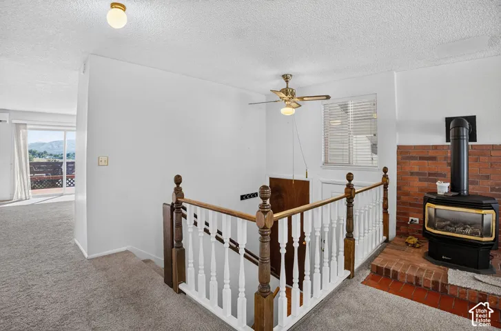 Built-in brick fireplace with a black wood-burning stove, wood staircase railing with white spindles, and a brass ceiling fan