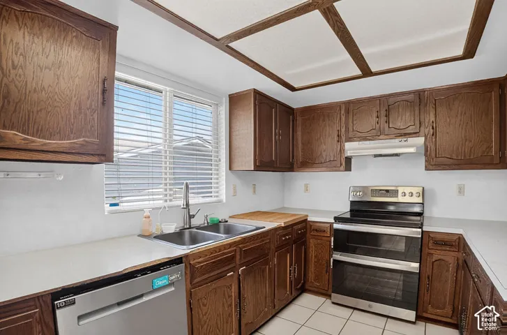 Kitchen featuring wood cabinetry, a stainless steel double oven range, a stainless steel dishwasher, a double basin sink, and ceiling-mounted light panels