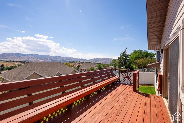 Expansive wood deck with built-in bench seating and decorative railing, featuring residential rooftops and a distant mountain range