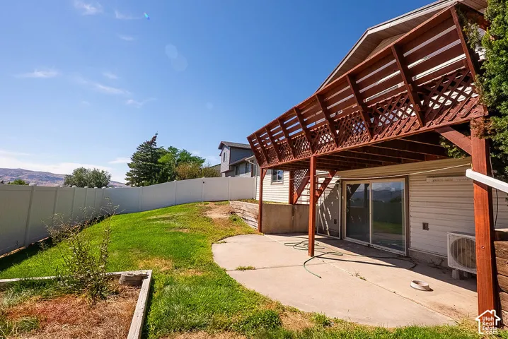 Spacious concrete patio with an overhead wood deck featuring lattice railing, sliding glass door access, and a fully fenced yard