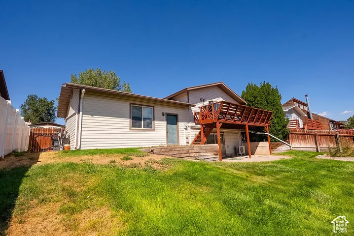 Expansive backyard featuring a multi-level wooden deck, a lower-level concrete patio, horizontal siding, and a white privacy fence