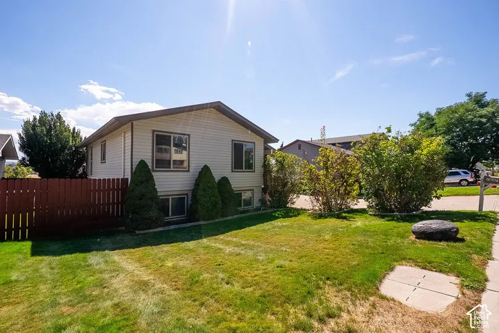 Split-level property featuring light-colored siding, a brown roof, and a red wood privacy fence