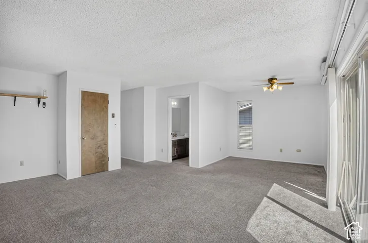 Spacious room featuring neutral carpeting, white walls, a ceiling fan with integrated lighting, and a prominent sliding glass door
