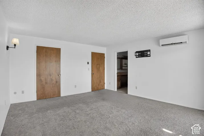 Wall-mounted sconce, light wood-finish doors, wall-mounted air conditioning unit, and gray carpet flooring