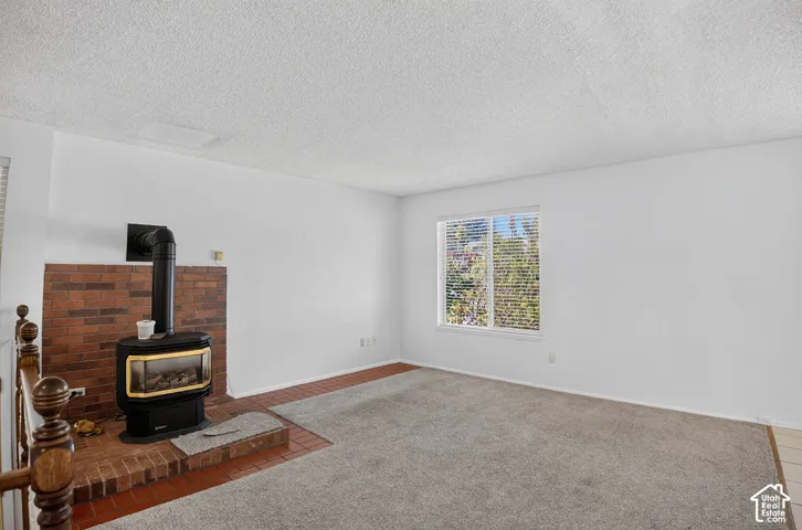 Wood-burning stove with a brick surround, large window with blinds, and carpeting