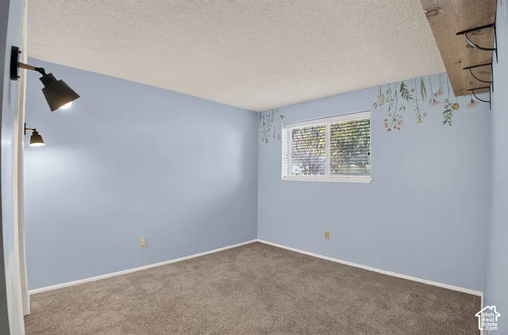 Carpeted flooring, window with blinds, wall-mounted light fixtures, textured ceiling, and built-in shelving