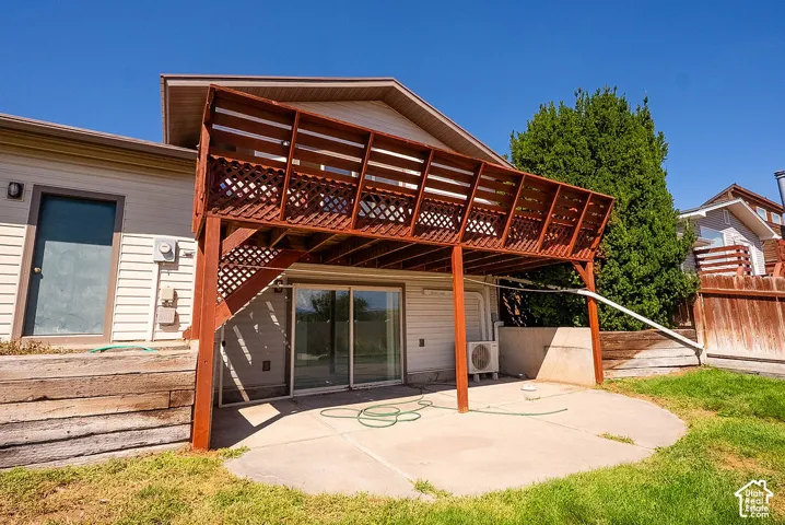 Upper-level wood deck with lattice railing, concrete patio, sliding glass door access, and a wood privacy fence