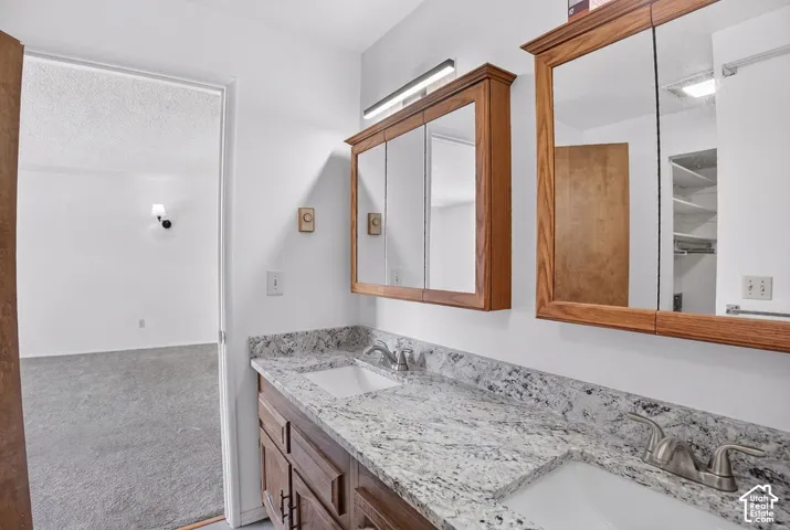 Dual vanity with integrated sinks, speckled stone-finish countertop, wood-finish cabinetry, and framed mirrored medicine cabinets