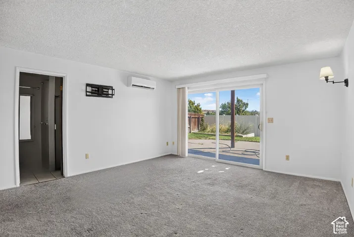 Sliding glass door, wall-mounted sconce, split-system air conditioning unit, wall-mounted television bracket, and light-colored carpeting