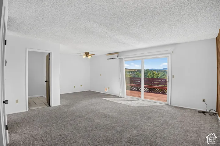 Expansive living area featuring gray carpeting, white walls, a ceiling fan, and sliding glass doors opening to a wood deck