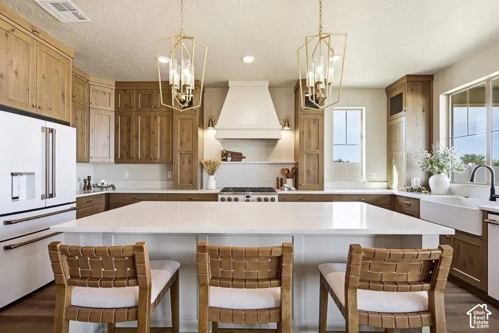 Spacious kitchen featuring an expansive island with a white countertop, wood-finish cabinetry, a large apron-front sink, and geometric pendant lighting