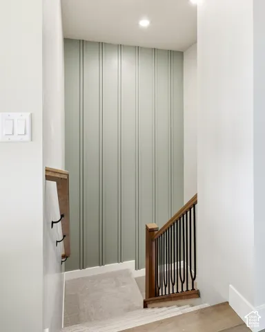 Wood-finish flooring leading to carpeted stairs with a wood and wrought iron handrail