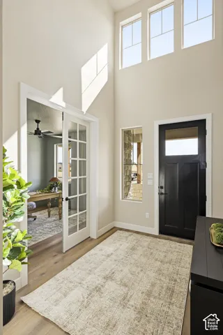 Two-story entry foyer with wood-finish flooring, a dark-paneled door, transom windows, and a French door entry to an additional room