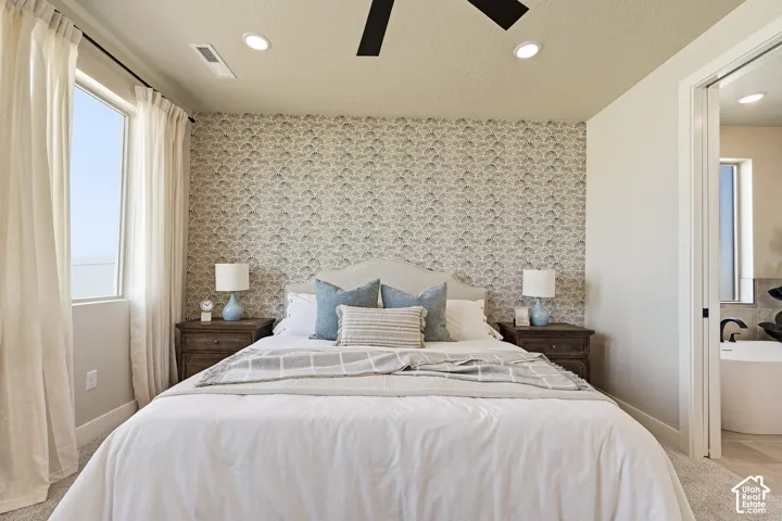 Recessed ceiling lights, ceiling fan, accent wall with patterned wallpaper, large window, and an adjacent bathroom with a freestanding tub