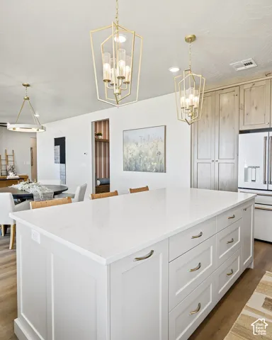 Central kitchen island with white countertop, light wood-finish flooring, and gold-tone pendant lighting