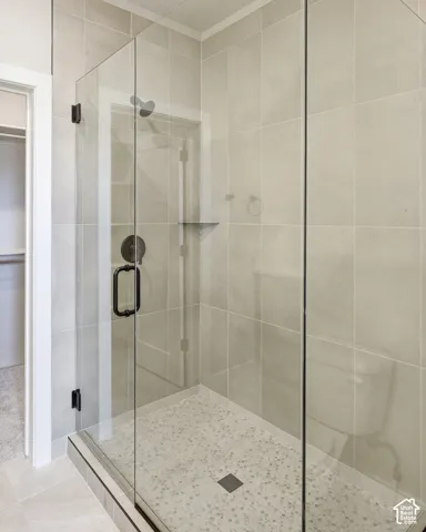 Glass-enclosed shower with a dark bronze showerhead, coordinating dark bronze hardware, a tiled shower bench, and a pebbled shower floor