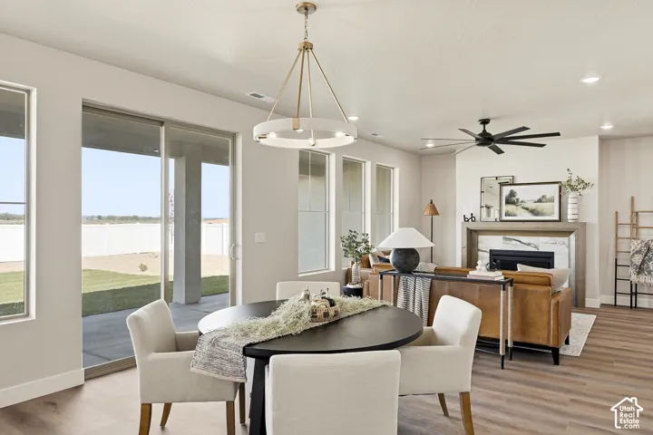 Open-concept living space with wood-finish flooring, a contemporary fireplace with a stone surround and wood mantle, a modern ceiling fan, and a gold-finish chandelier