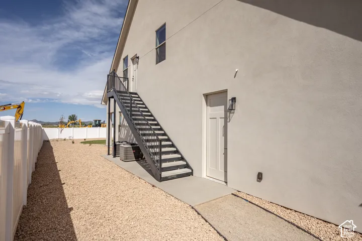 Stucco exterior with a metal exterior staircase, a privacy fence, and a gravel yard
