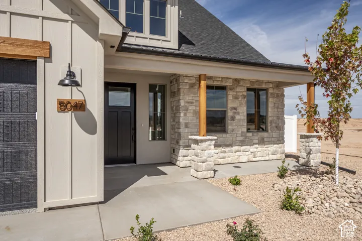 Board and batten siding, stone facade, covered porch with wood columns, dark entry door with transom window, and a dark asphalt shingle roof