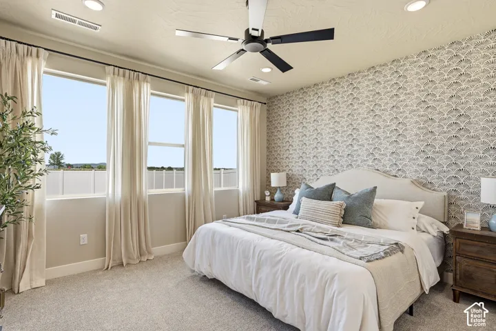 Serene primary bedroom showcasing a neutral color palette with patterned accent wall, ceiling fan with integrated lighting, and triple-window configuration with floor-to-ceiling drapery