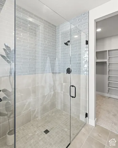 Glass-enclosed walk-in shower with light blue subway tile and beige square tiles