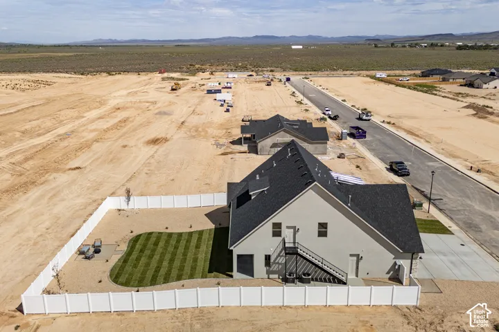 Newly constructed residence featuring a gray exterior, dark shingle roof, and a private fenced backyard with a manicured lawn