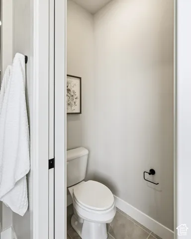 Recessed lighting illuminates this powder room featuring a white toilet, light gray walls, and a matching tile floor