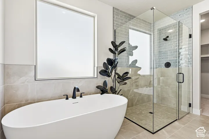 Freestanding soaking tub with matte black fixtures, glass-enclosed shower, light blue subway tile, and large format floor tiling