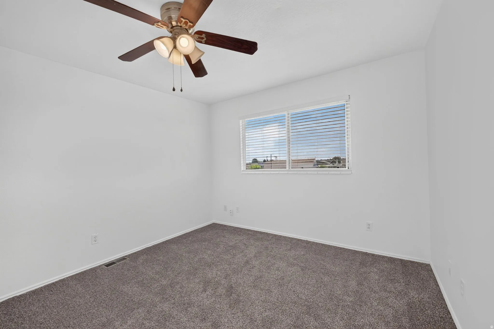 Neutral wall finishes with a ceiling fan light fixture, dual pane window with blinds, and carpeted flooring