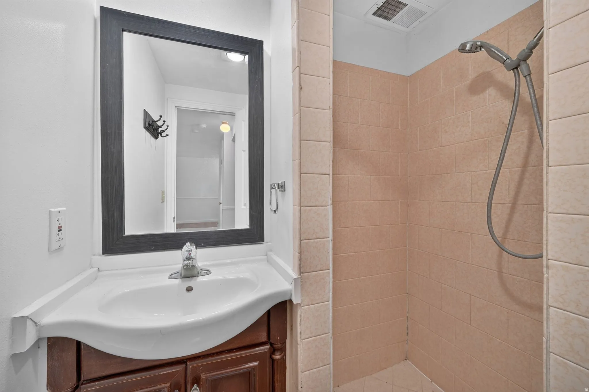 Bathroom featuring a vanity with a white countertop and basin, wood-finish cabinetry, a framed mirror, and a shower with tiled walls
