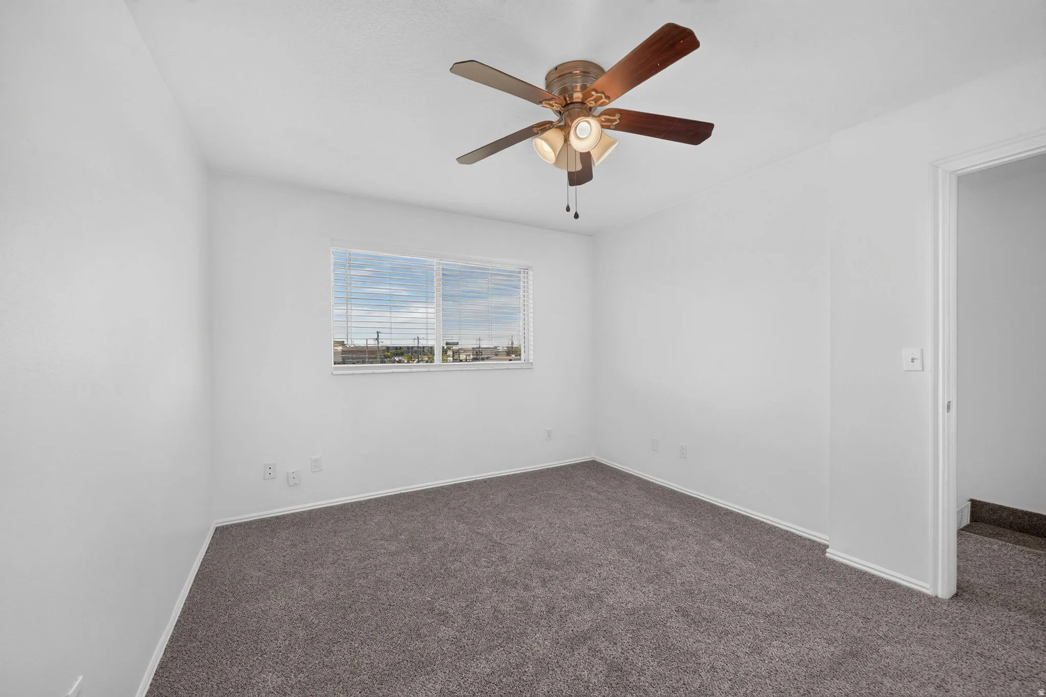 Neutral wall paint, ceiling fan with integrated lighting, window with blinds, and grey carpeting