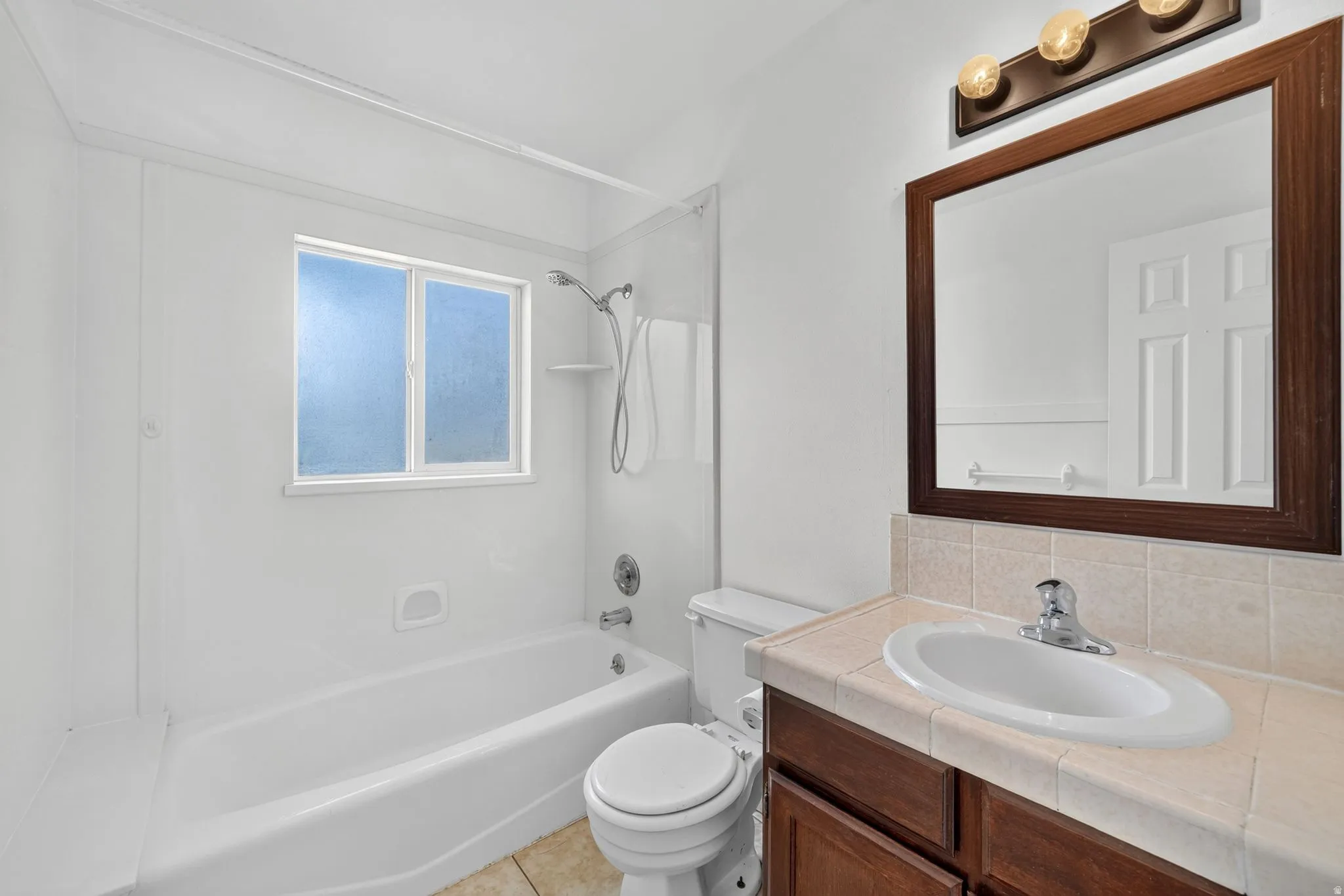 White bathtub/shower combination with a frosted window, chrome fixtures, and a shower shelf
