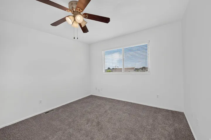 Neutral wall finishes with a ceiling fan light fixture, dual pane window with blinds, and carpeted flooring