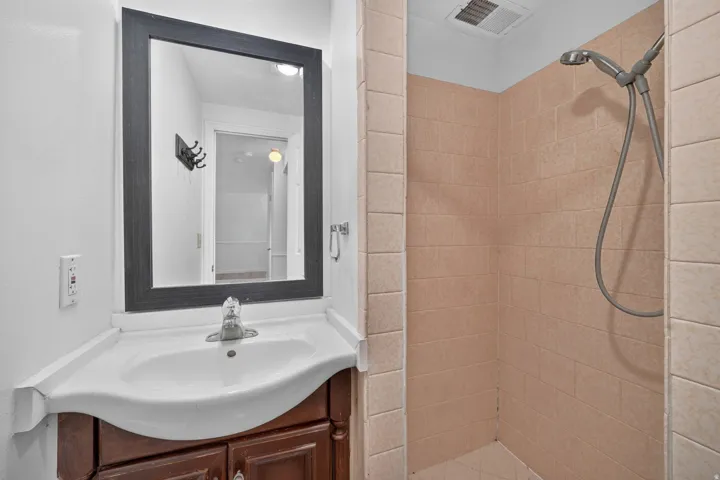 Bathroom featuring a vanity with a white countertop and basin, wood-finish cabinetry, a framed mirror, and a shower with tiled walls